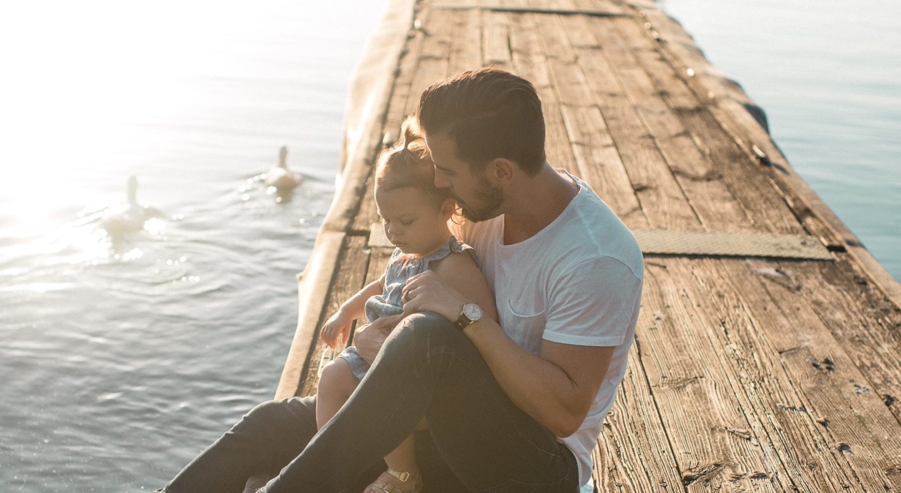 Dad holding toddler daughter sitting on lake pier