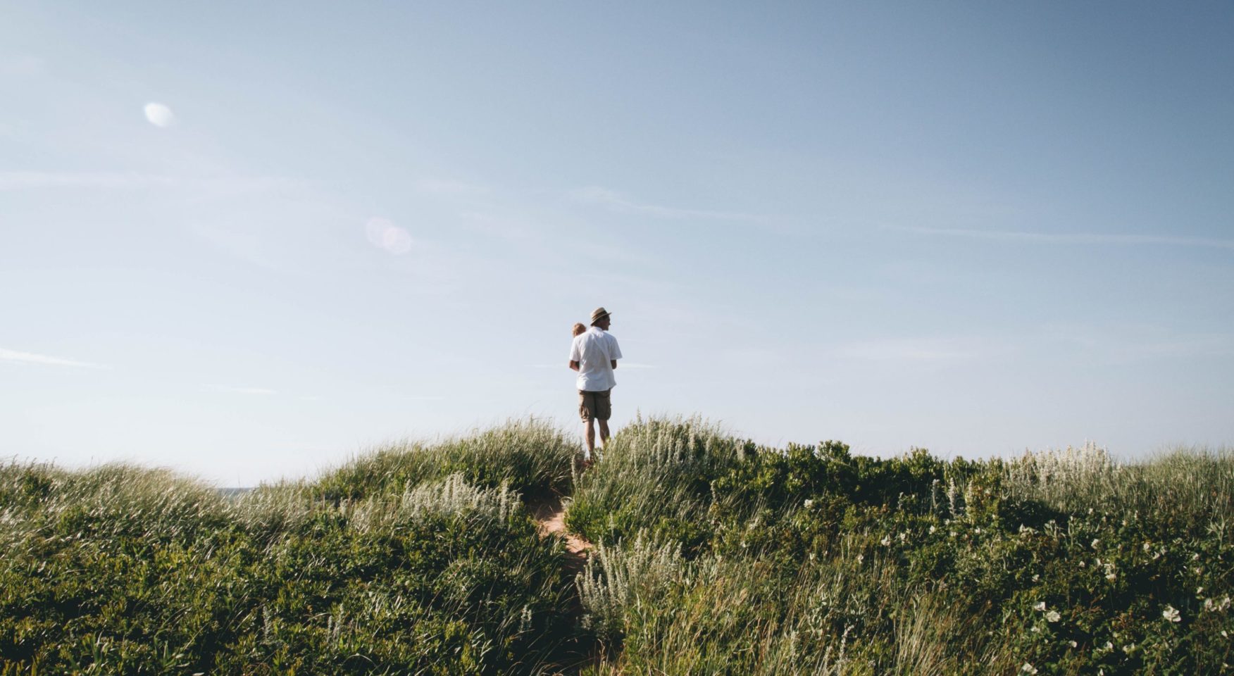 Father and baby standing on beach dune