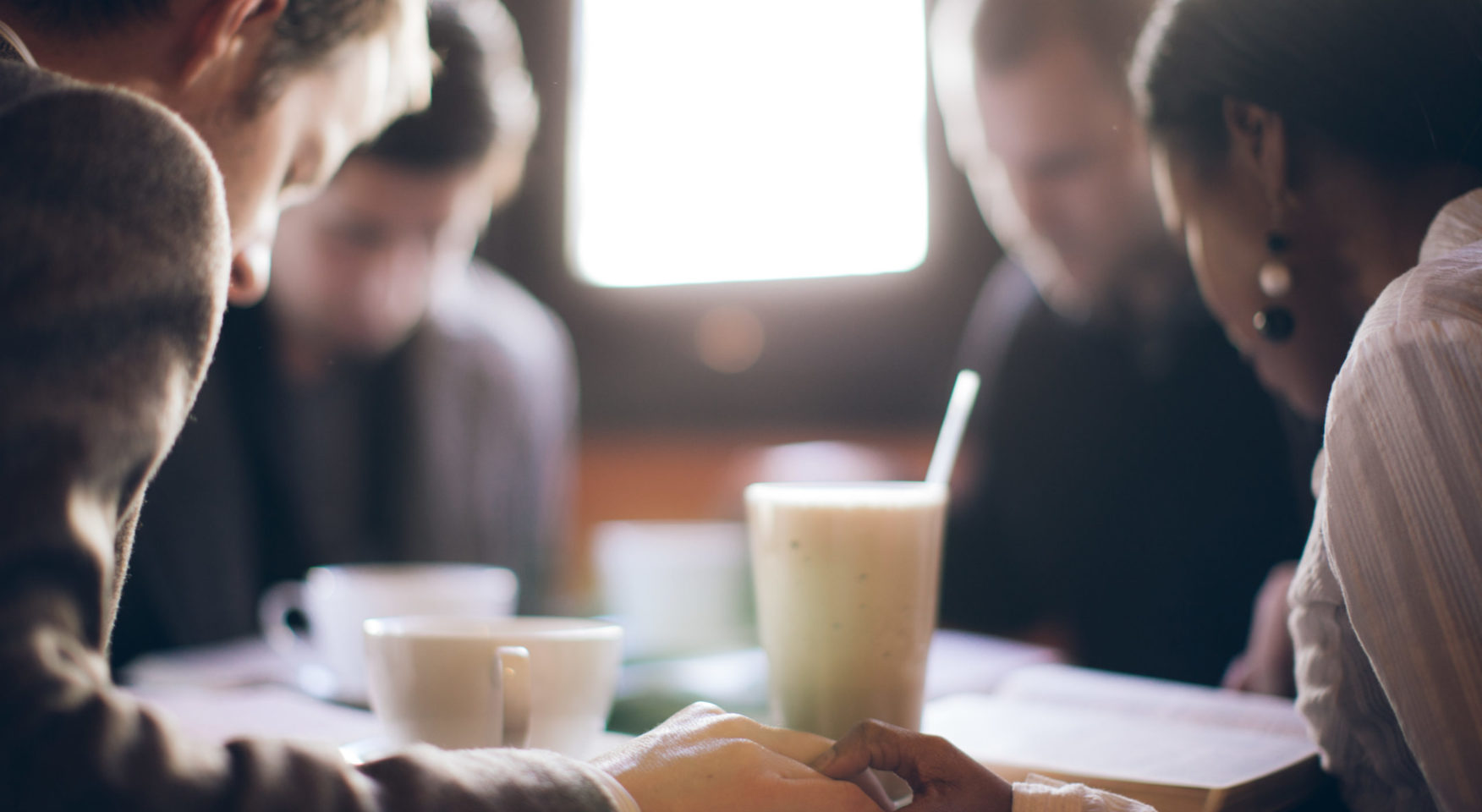 Group of people praying at table with milkshake