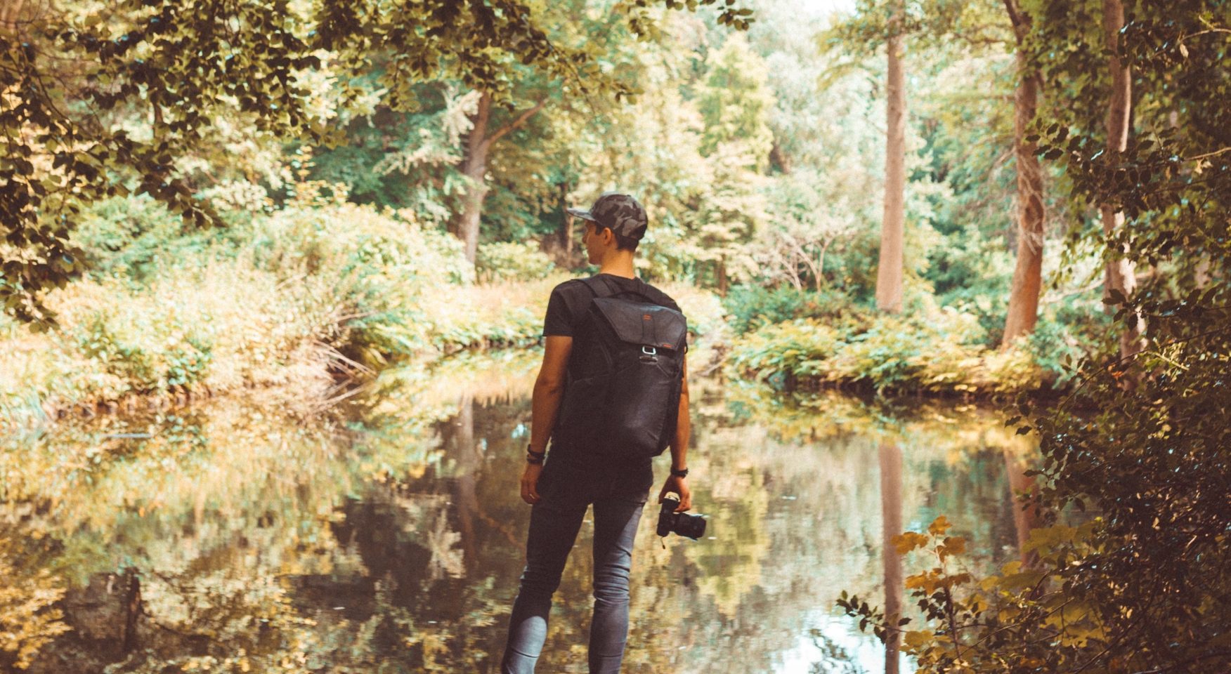 Man wearing backpack and holding camera walking through swamp