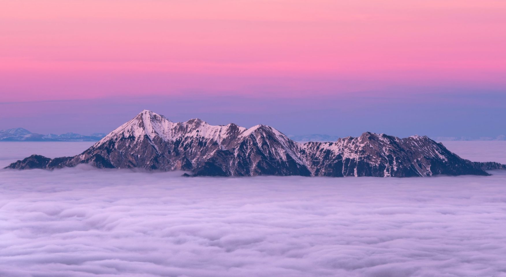 Rocky mountain tops peeking through clouds against briight purple pink sky