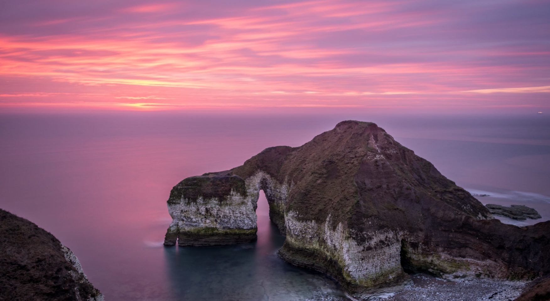 rocky coast on the ocean with purple pink sky