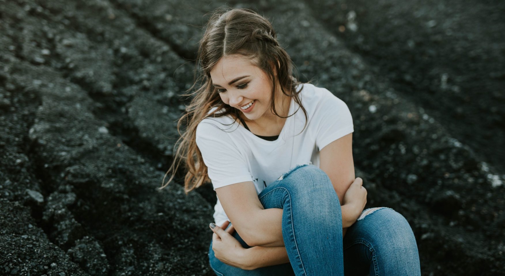 young woman sitting on rocks hugging knee